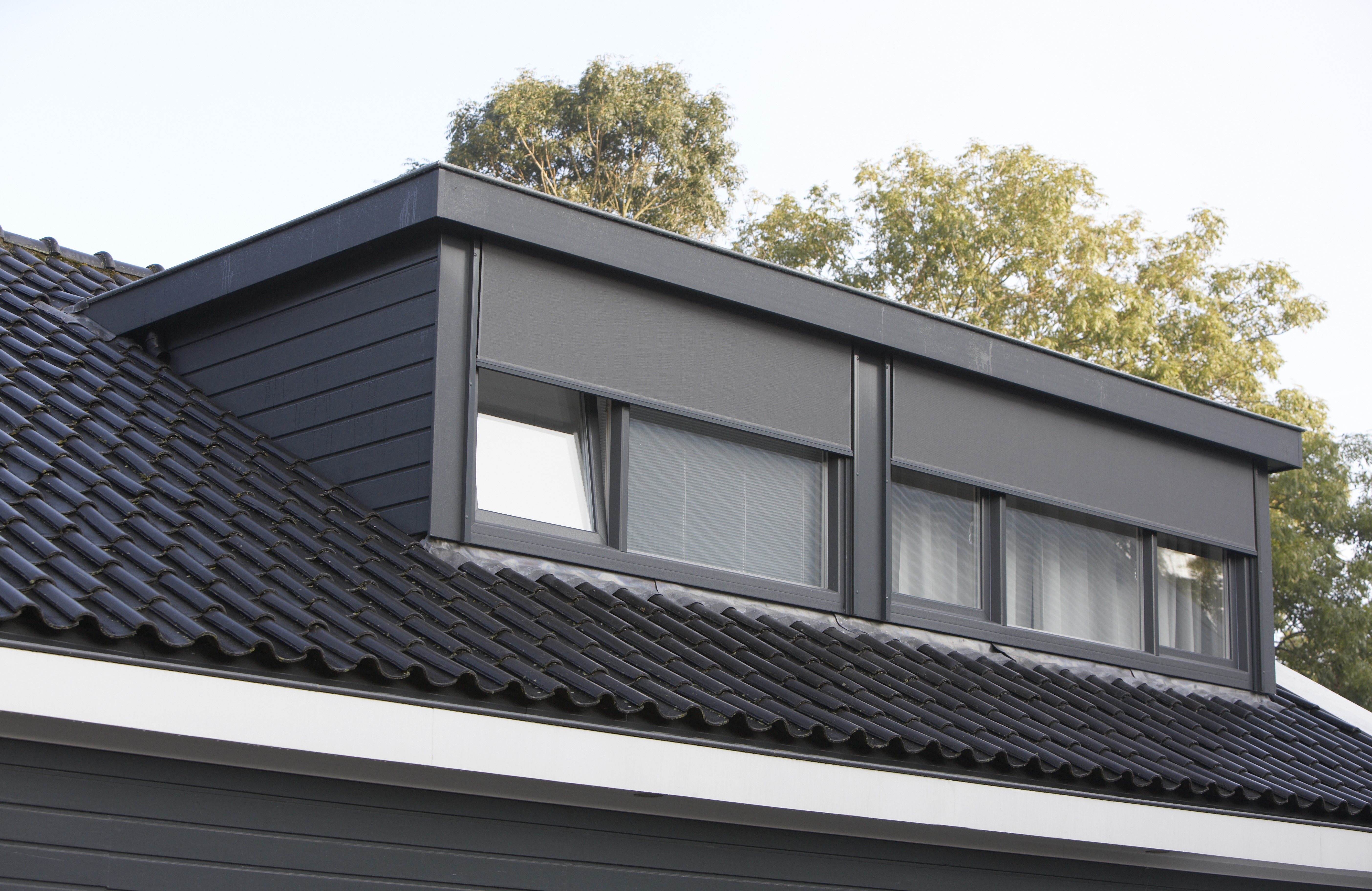 Zwarte dakkapel vanaf 6 meter, met houtnerf op zwart dak. Zwarte rolluik voor het raam voor zonwering.